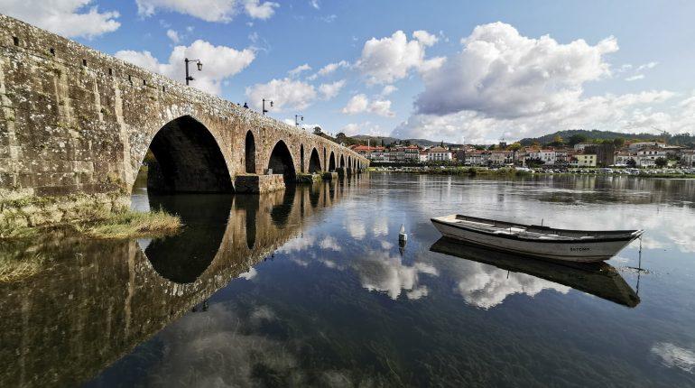 white wooden row boat on clear water near bridge under blue sky and white clouds during day time