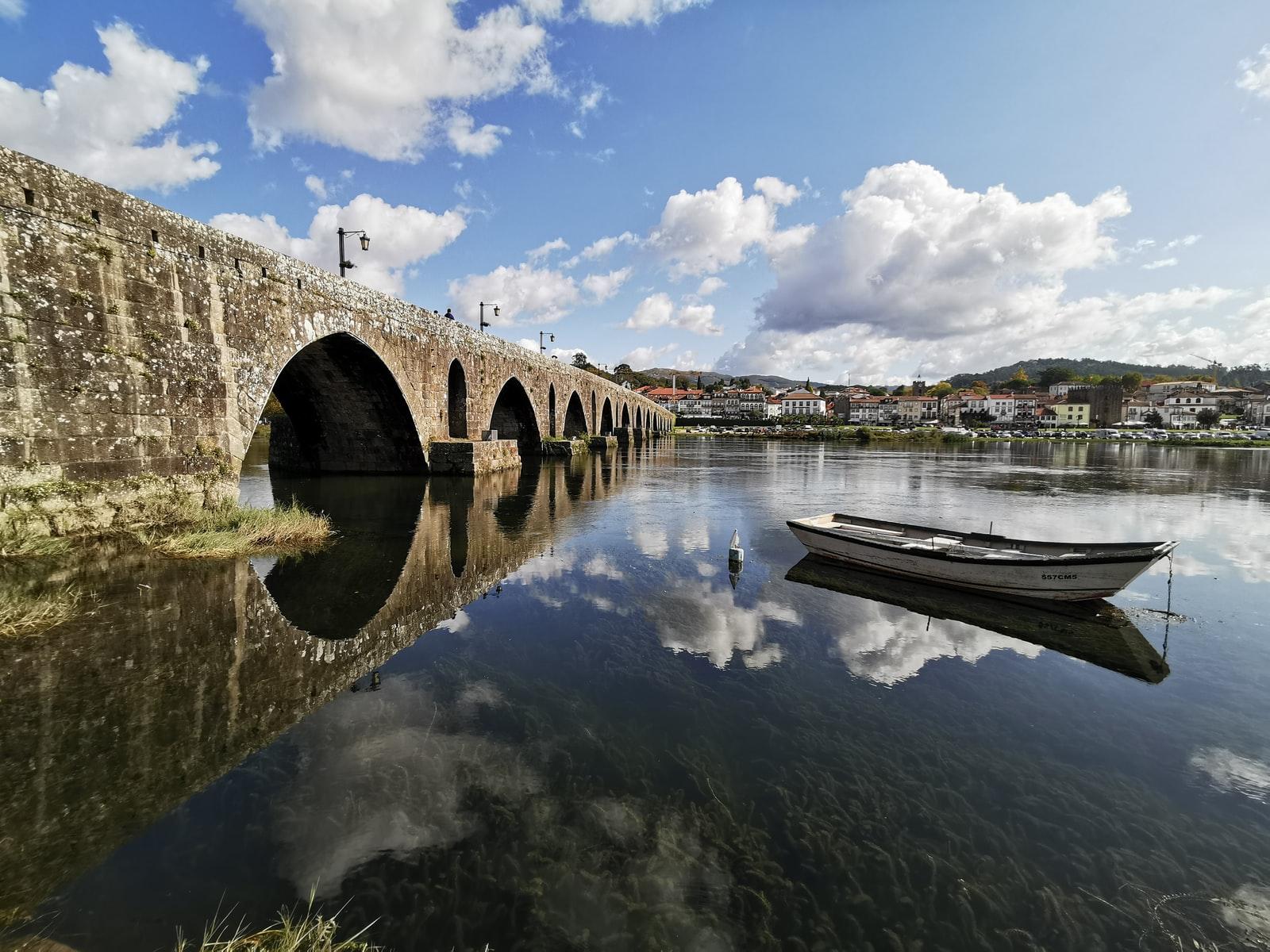 white wooden row boat on clear water near bridge under blue sky and white clouds during day time