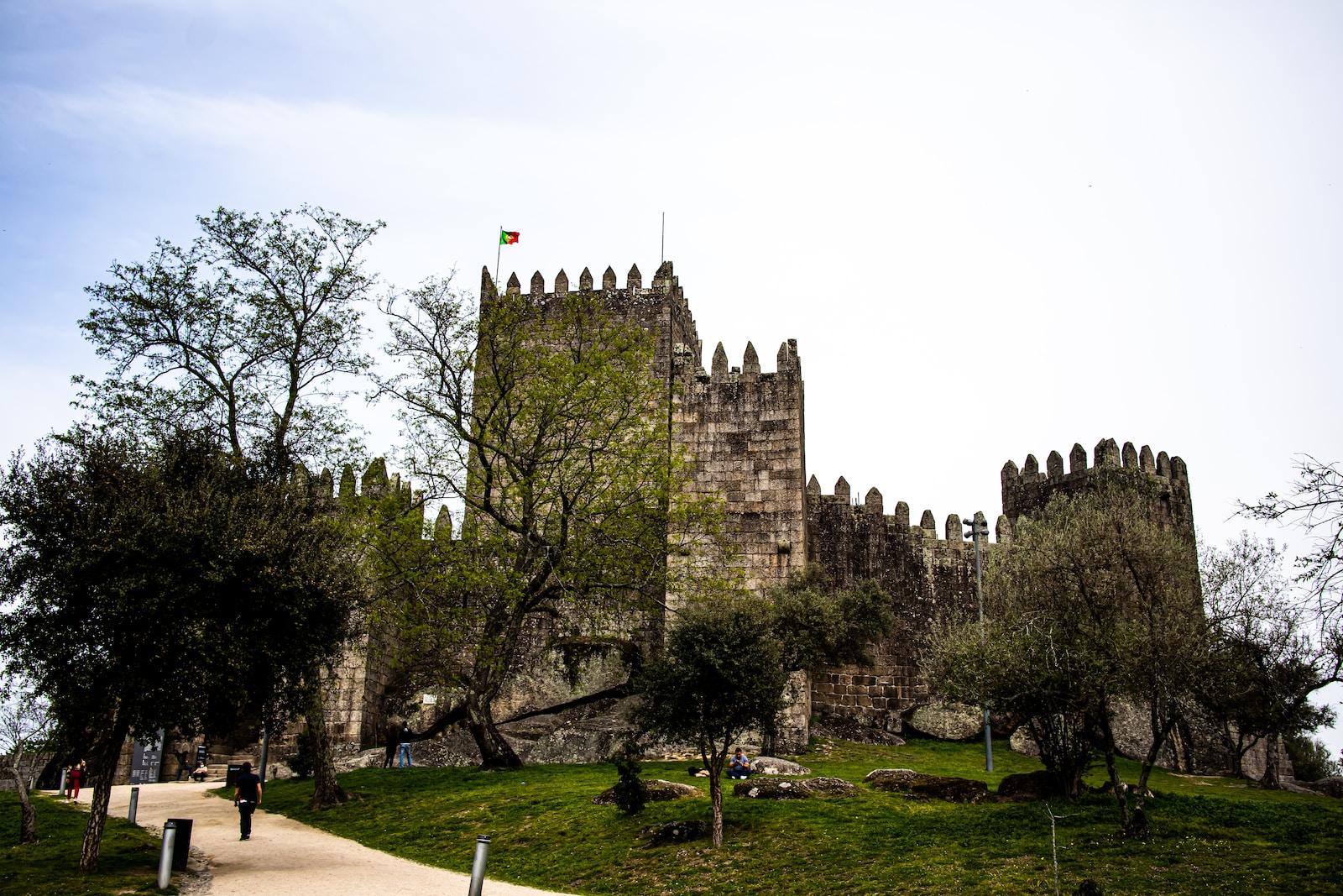 a castle with trees and grass with Guimarães Castle in the background