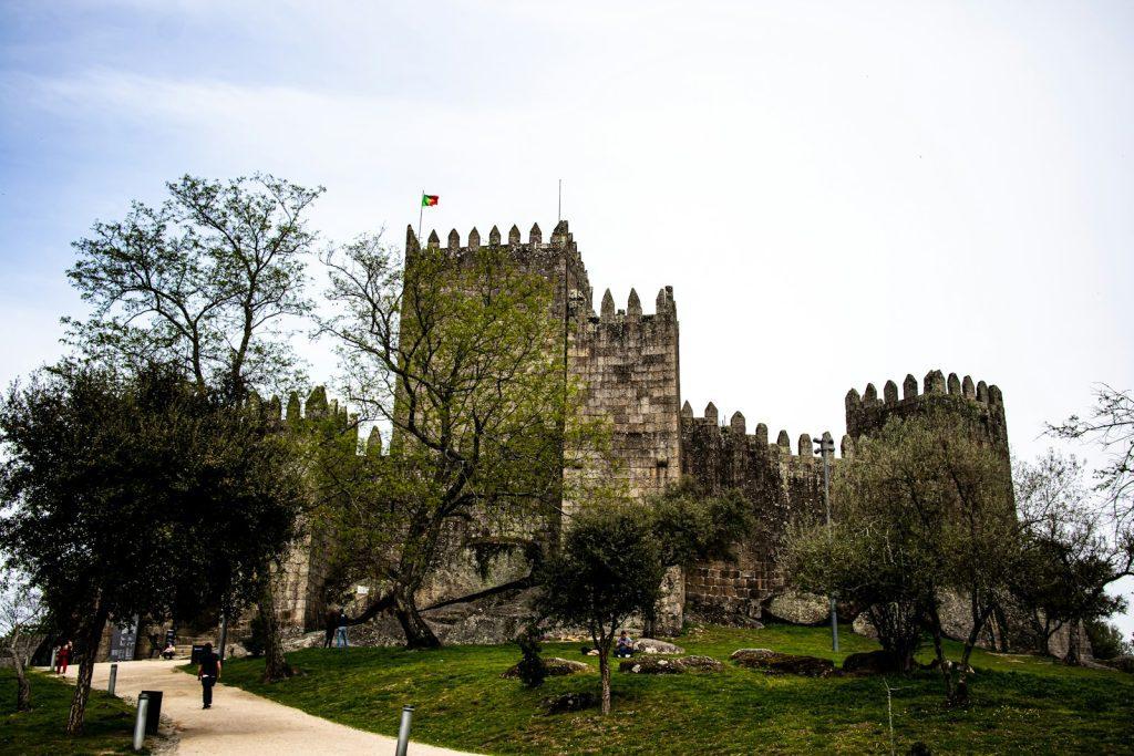 a castle with trees and grass with Guimarães Castle in the background
