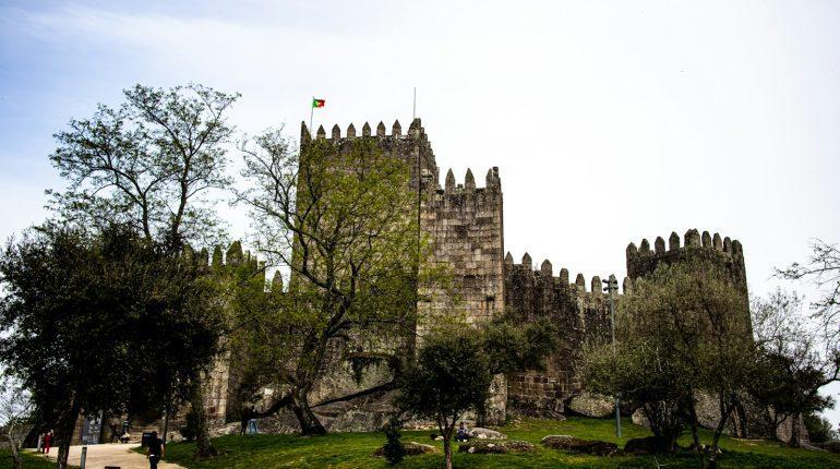 a castle with trees and grass with Guimarães Castle in the background