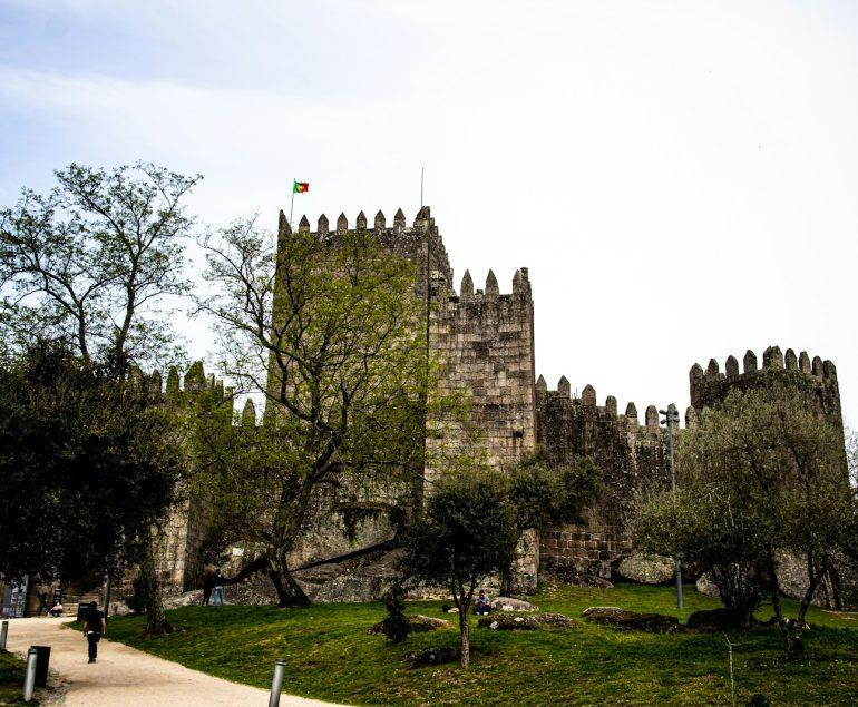 a castle with trees and grass with Guimarães Castle in the background